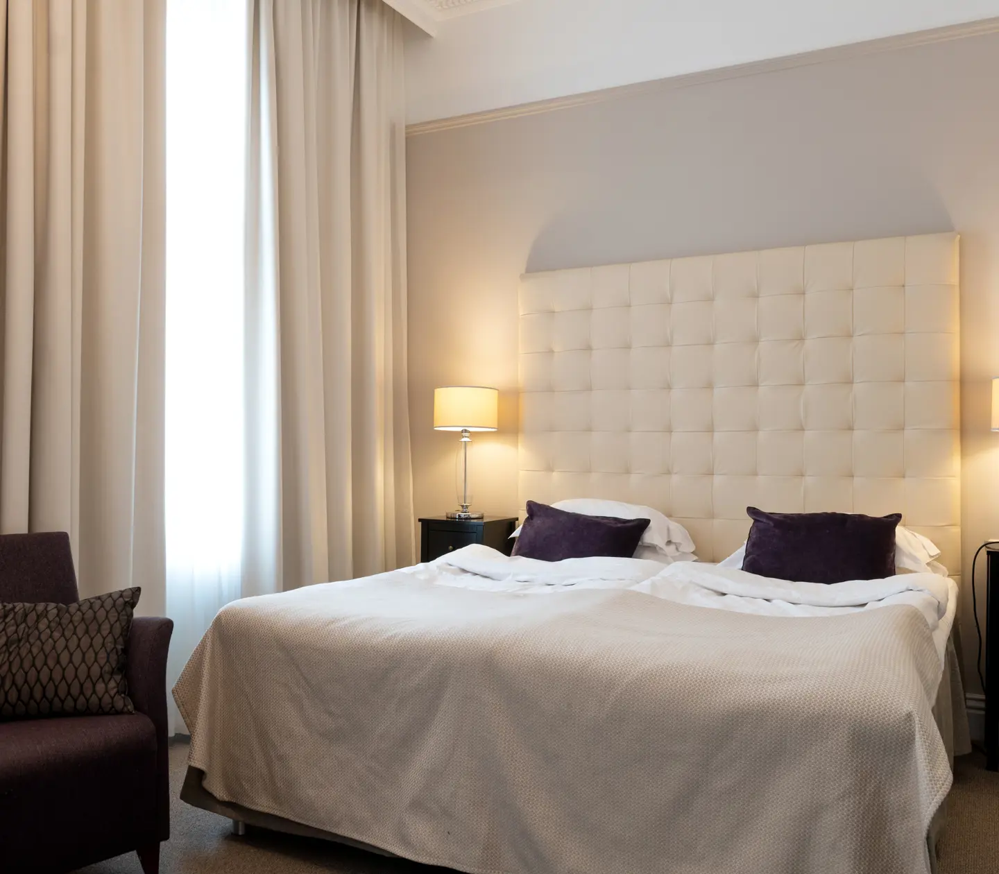 Ljust hotellrum med säng, vit sänggavel och fåtölj