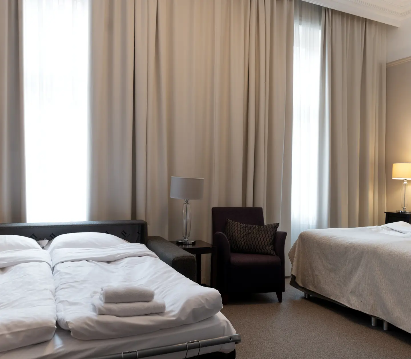 Ljust hotellrum med säng, fåtölj och utbäddad bäddsoffa