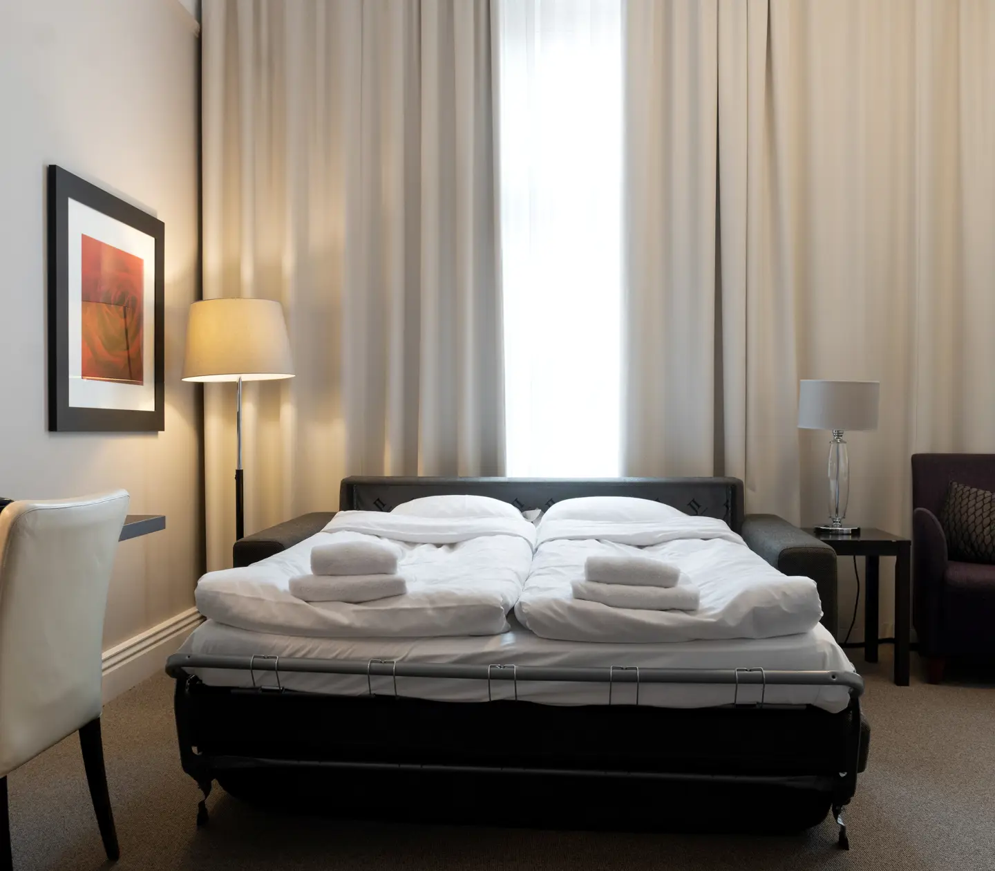 Ljust hotellrum med skrivbord, fåtölj och utbäddad bäddsoffa