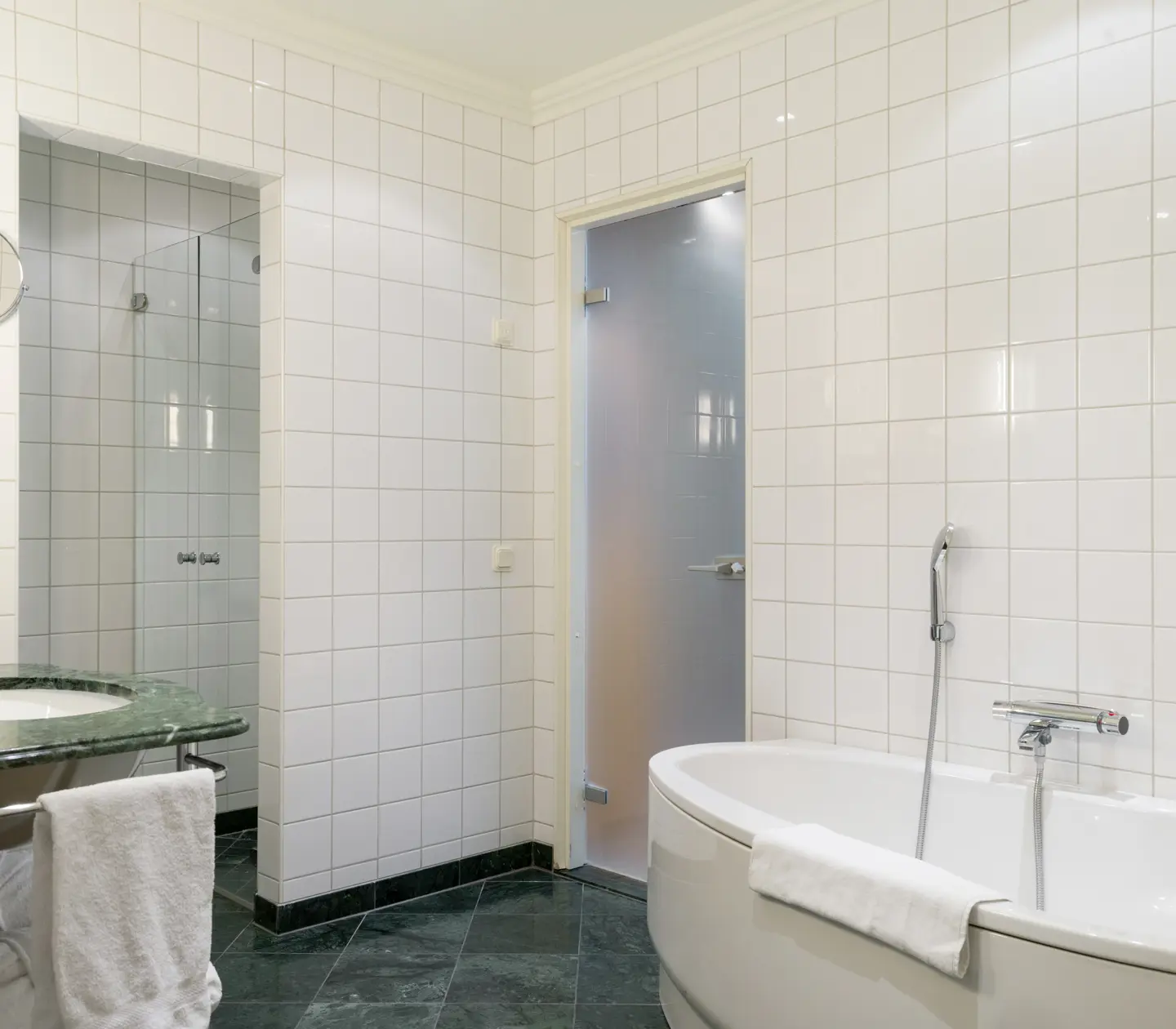 Ljust badrum med badkar, grönt handfat och handdukar
