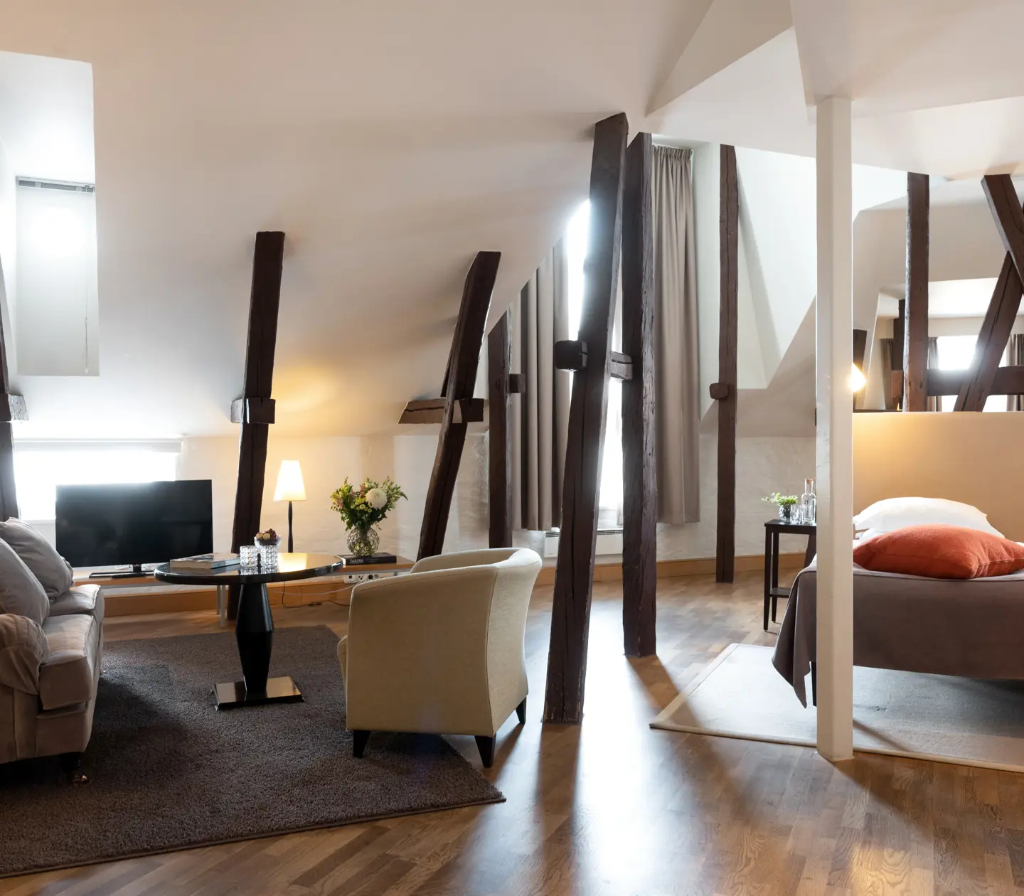 Hotellsvit med säng, soffgrupp och träbalkar från taket