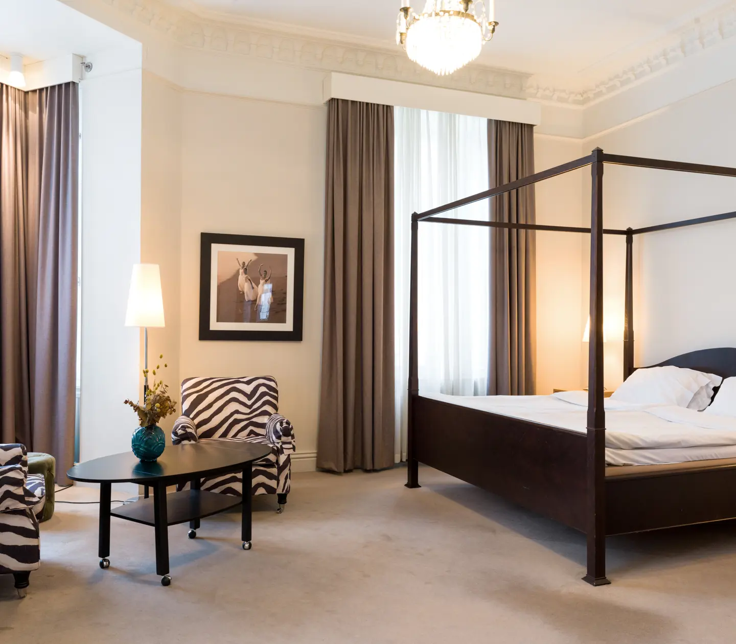Hotellsvit med säng, mörk sängram och fåtöljer