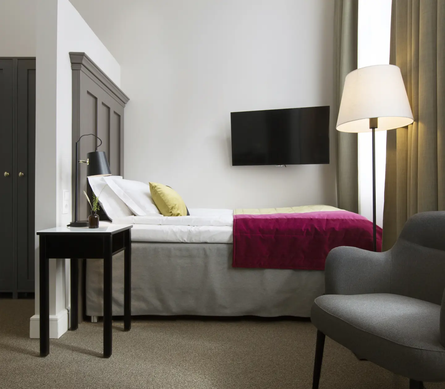 Ljust hotellrum med säng, garderob och fåtölj
