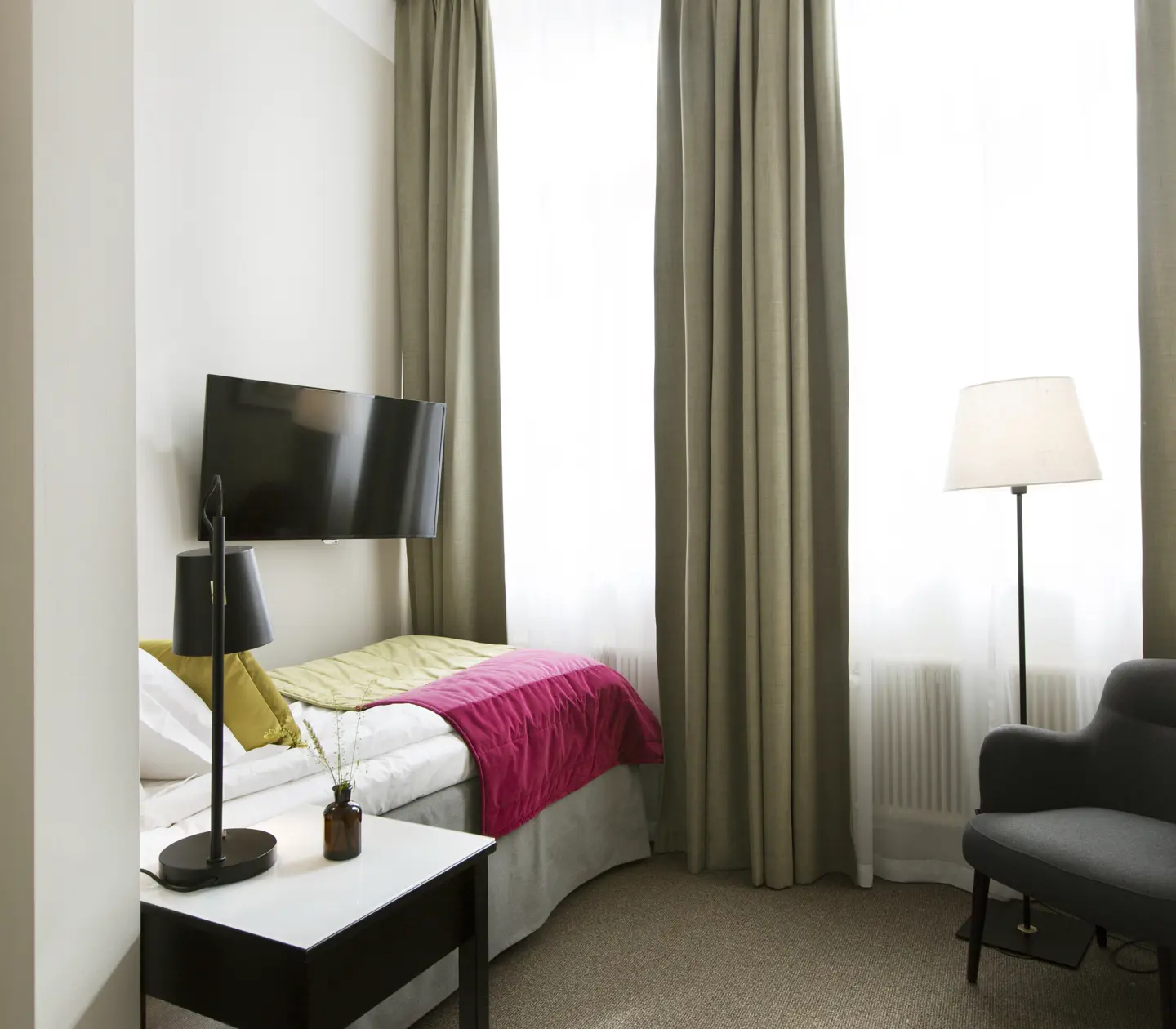 Ljust hotellrum med säng, tv och fåtölj