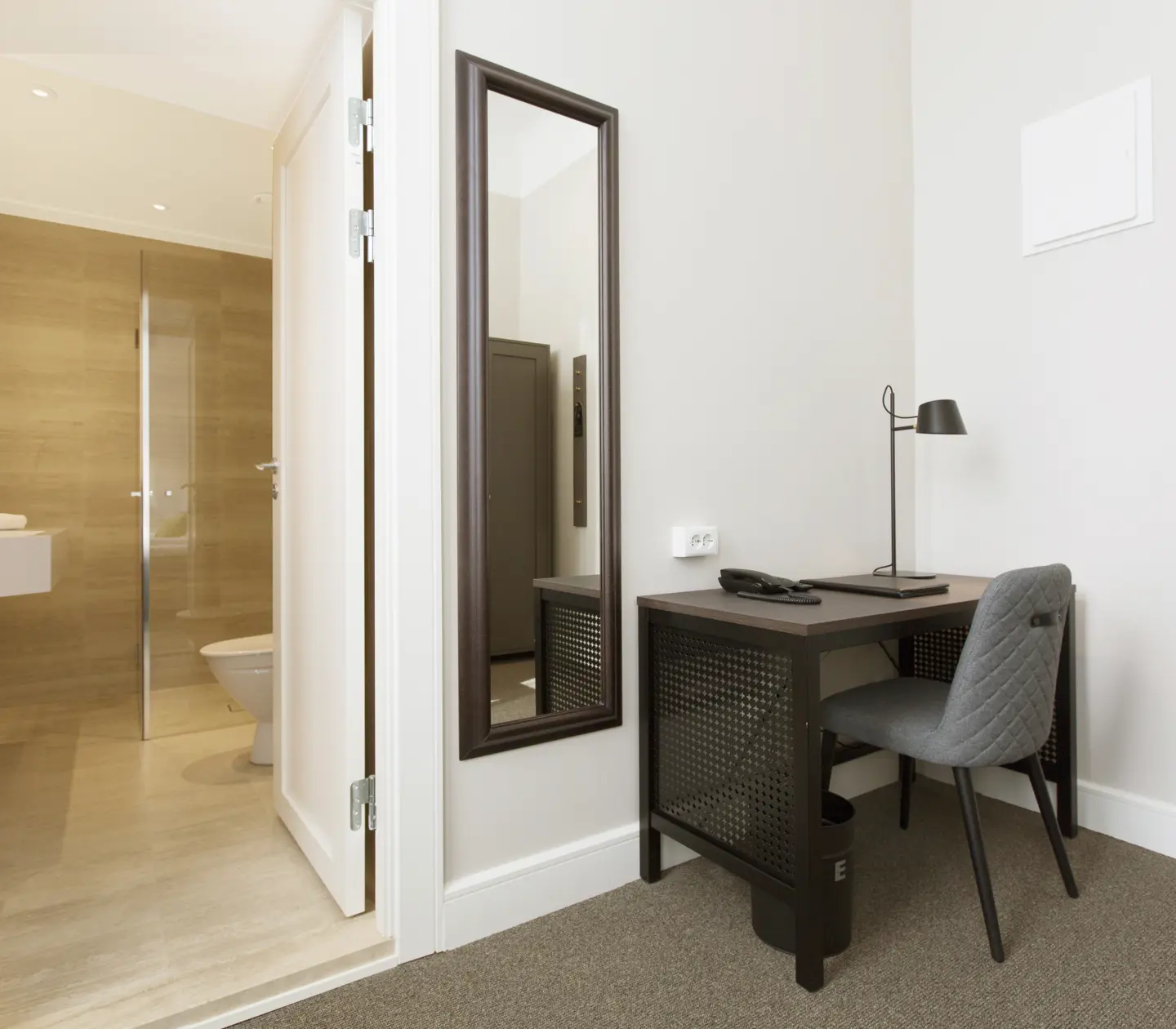 Ljust hotellrum med skrivbord, spegel och badrumsdörr