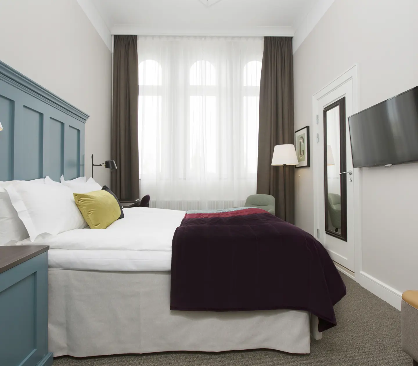 Ljust hotellrum med säng, stor blå sänggavel och tv