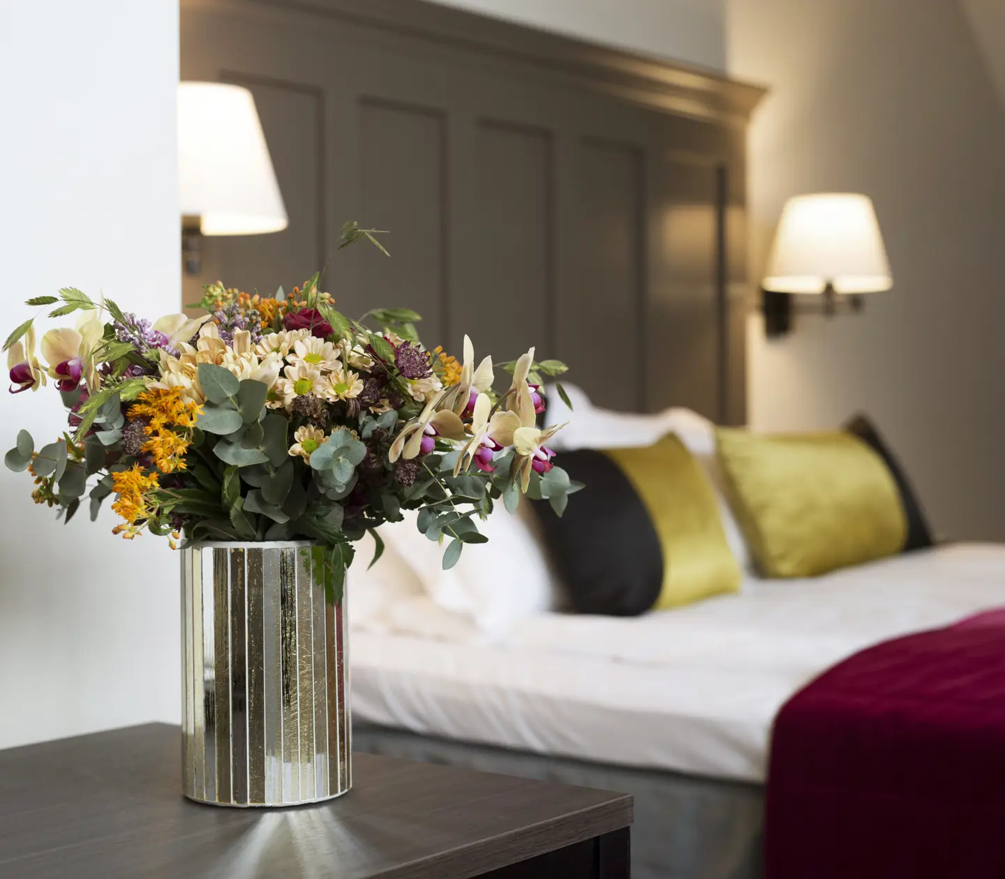 Ljust hotellrum med säng, blombukett och sänglampor