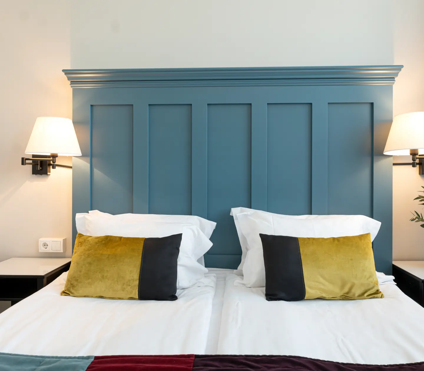 Ljust hotellrum med säng, stor blå sänggavel och sänglampor