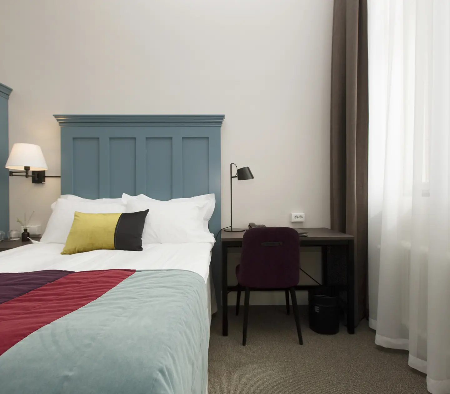 Ljust hotellrum med säng, blombukett och sänglampor