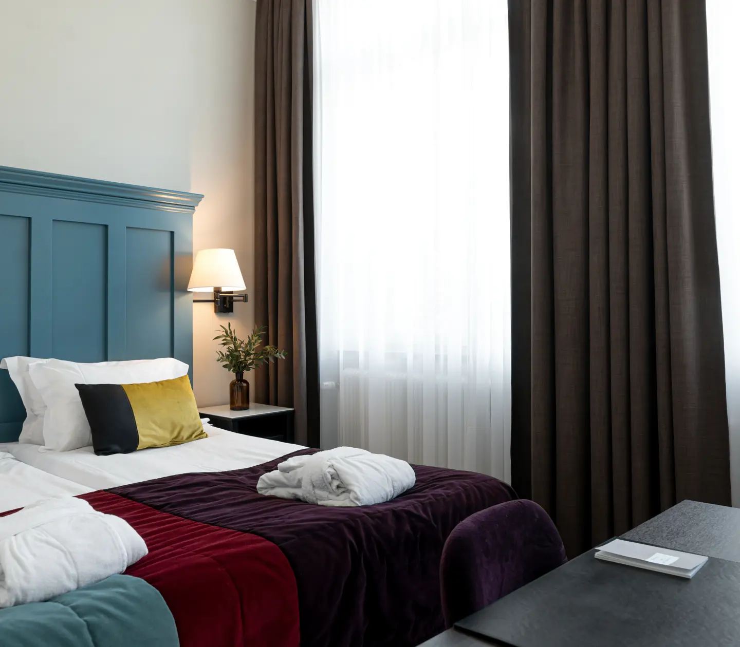 Ljust hotellrum med säng, stor blå sänggavel och morgonrockar