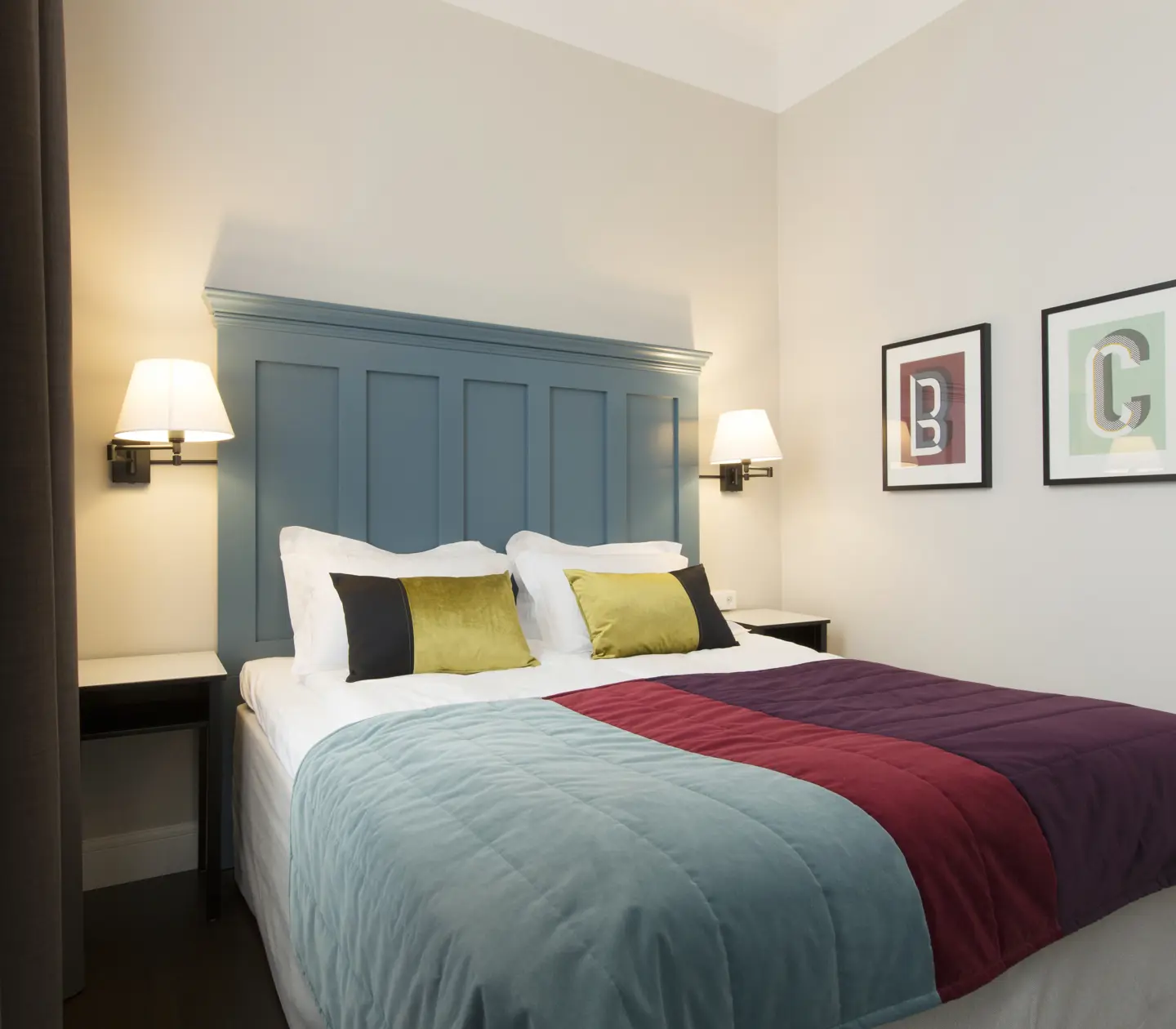 Ljust hotellrum med säng, stor blå sänggavel och sängtavlor