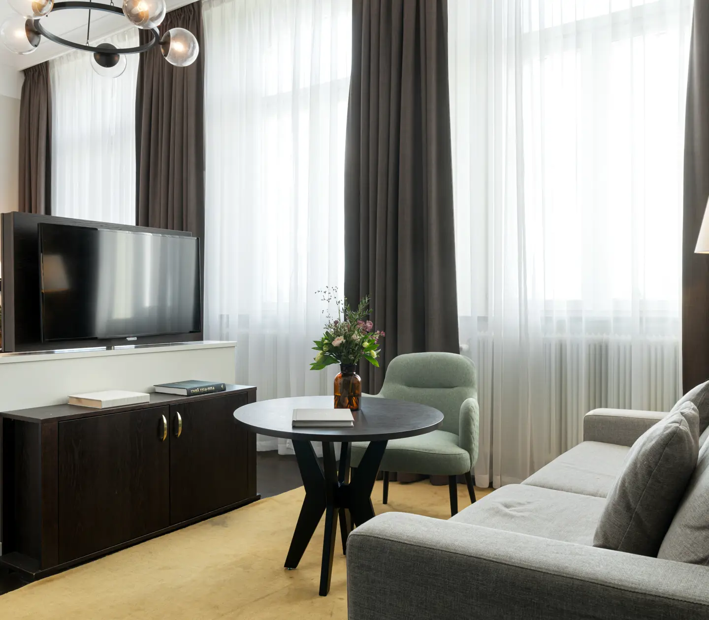 Ljust hotellrum med soffgrupp, tv och stora fönster