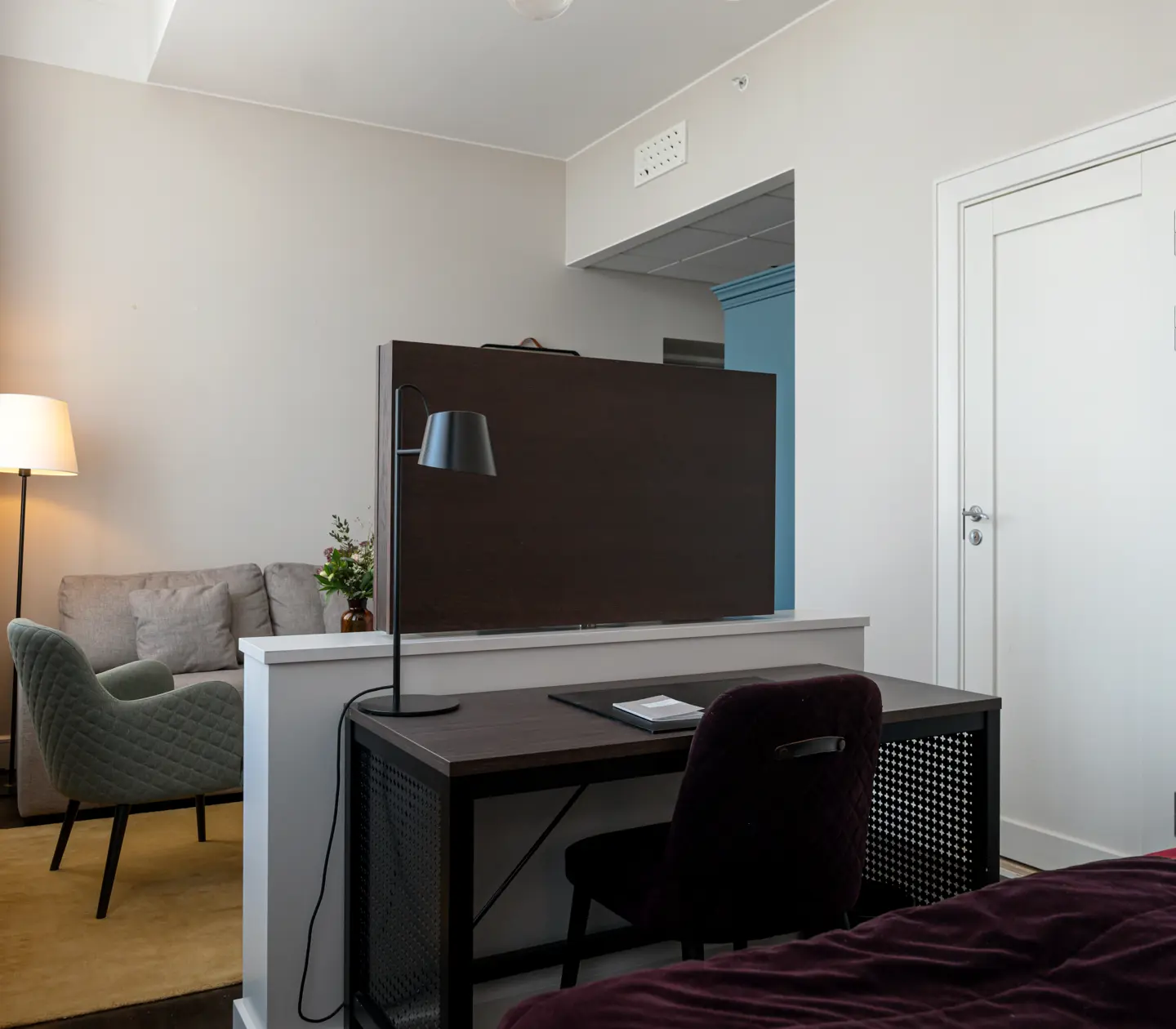 Ljust hotellrum med soffgrupp, tv och skrivbord