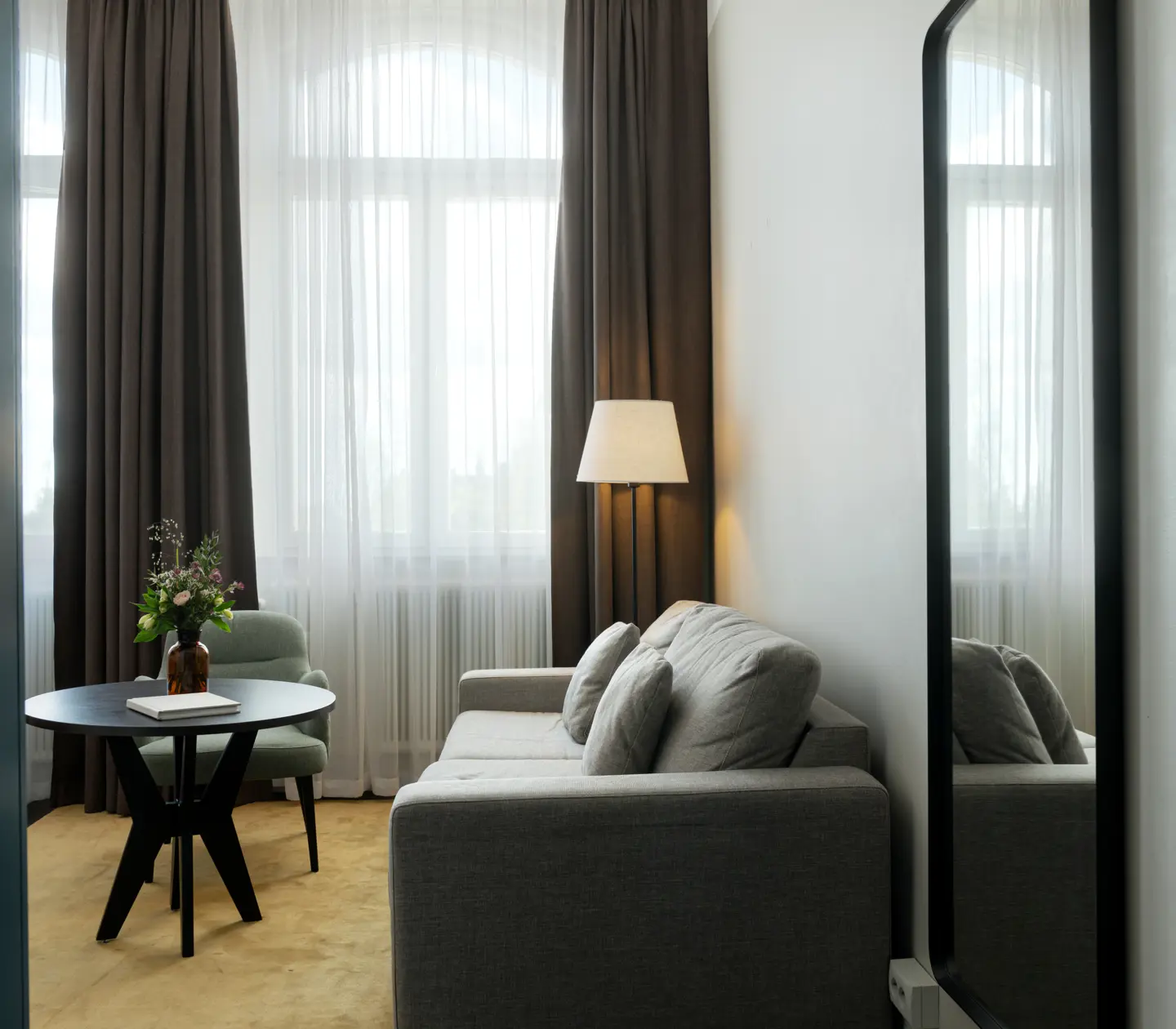 Ljust hotellrum med soffgrupp, spegel och garderob