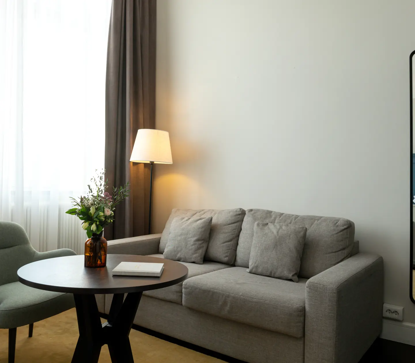 Ljust hotellrum med soffgrupp, spegel och fönster