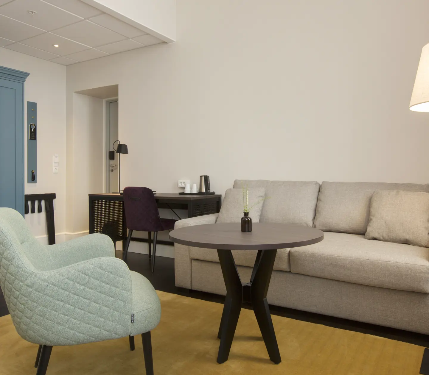 Ljust hotellrum med soffgrupp, skrivbord och garderob