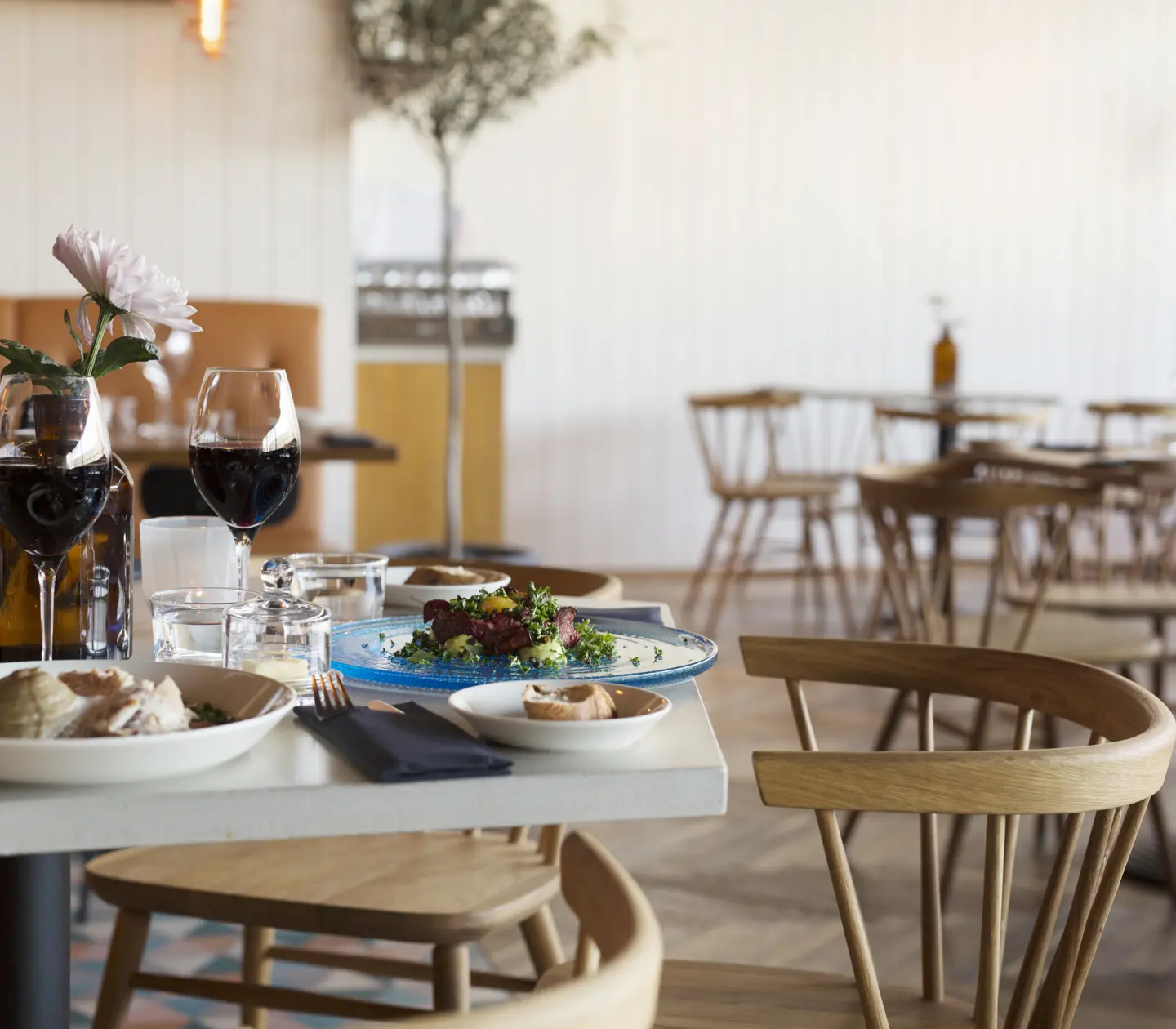 Restaurangmiljö med mat och vin serverad på bord och matgrupper i bakgrunden