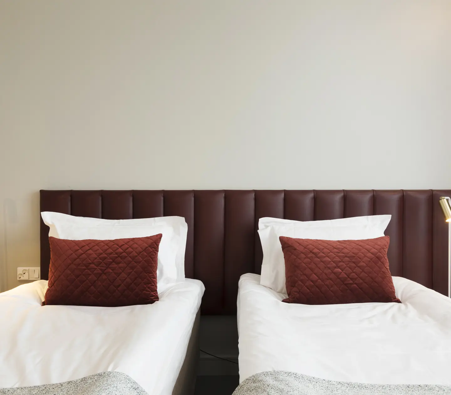 Ljust hotellrum med två enkelsängar bredvid varandra, vinröd sänggavel och små sänglampor