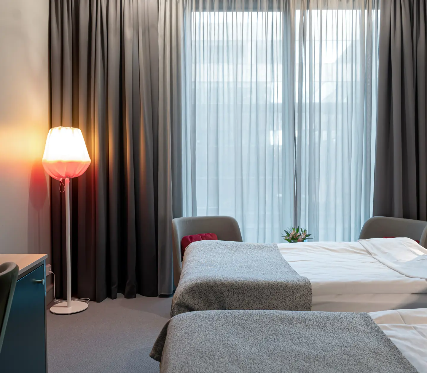 Ljust hotellrum med två enkelsängar bredvid varandra, skrivbord och fönster