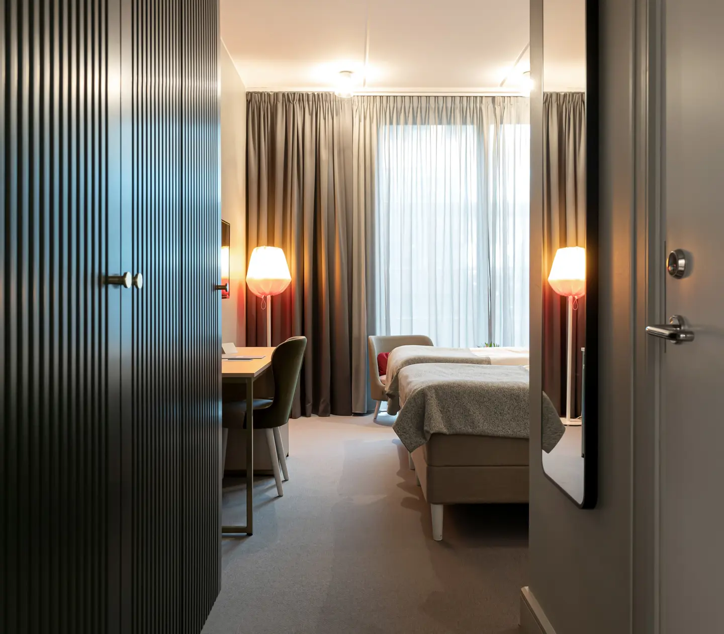Ljust hotellrum med två enkelsängar bredvid varandra, skrivbord och garderob