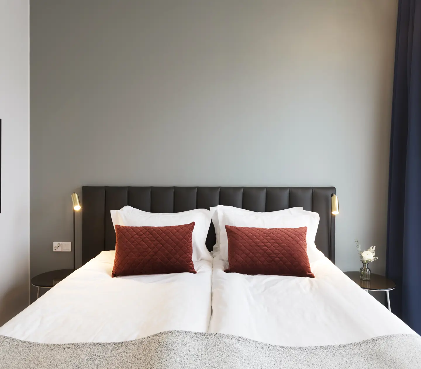 Ljust hotellrum med säng, mörk sänggavel och små sänglampor