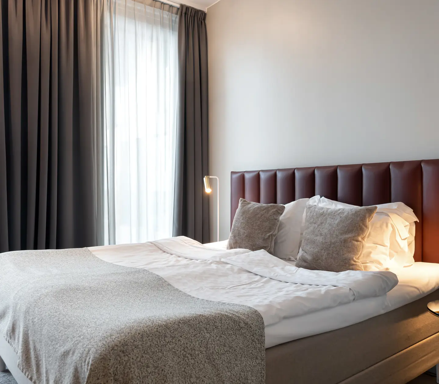 Ljust hotellrum med säng, vinröd sänggavel och fönster