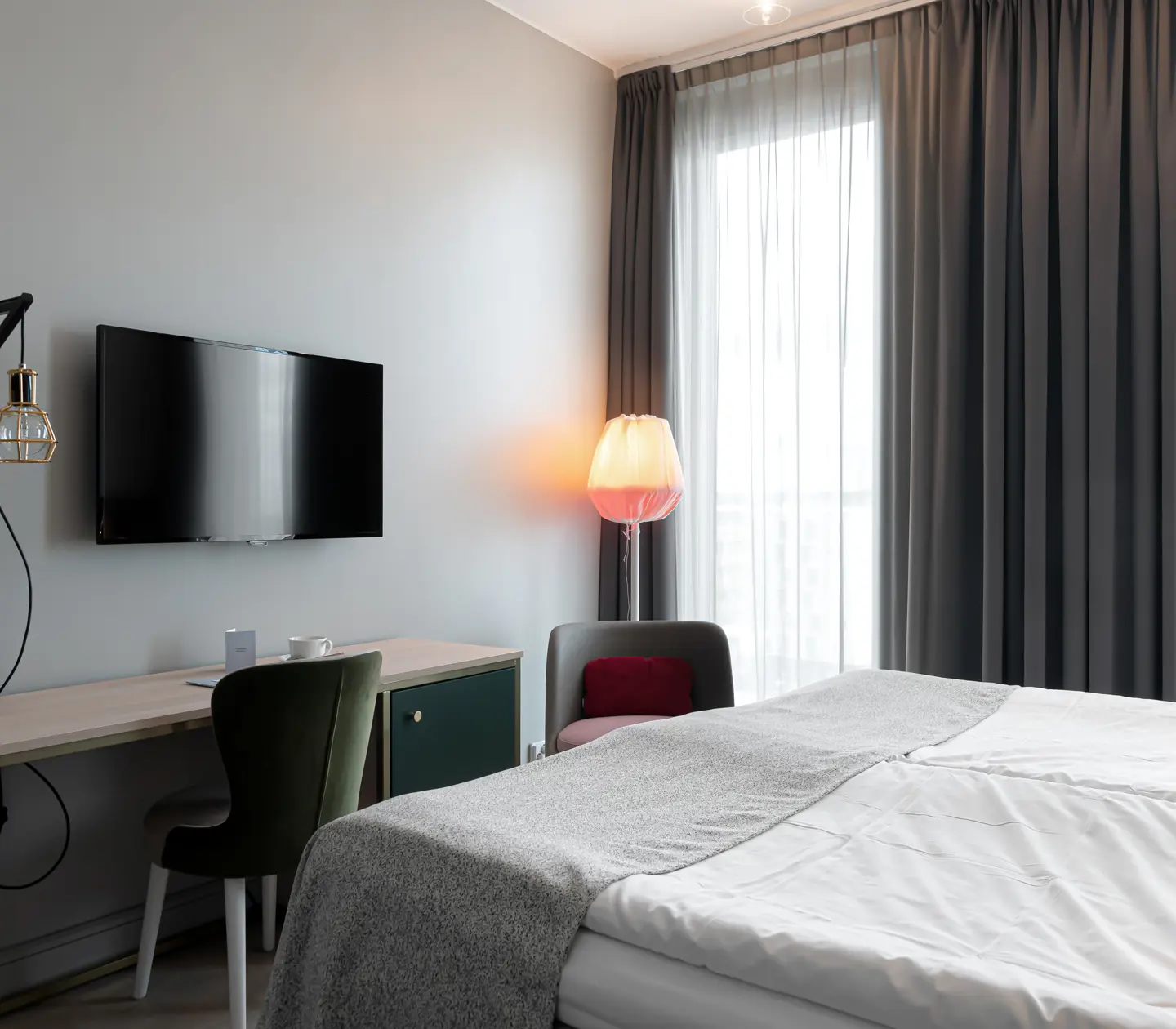 Ljust hotellrum med säng, skrivbord och tv