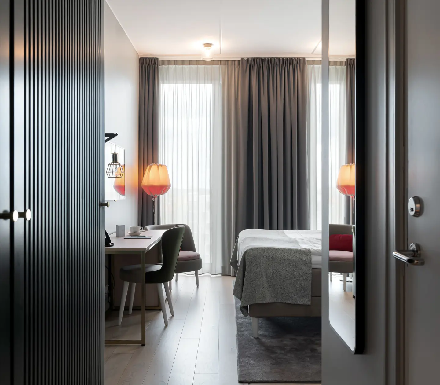Ljust hotellrum med säng, skrivbord och stort fönster