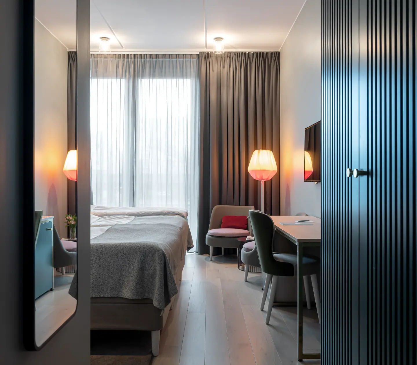 Ljust hotellrum med säng, garderob och skrivbord