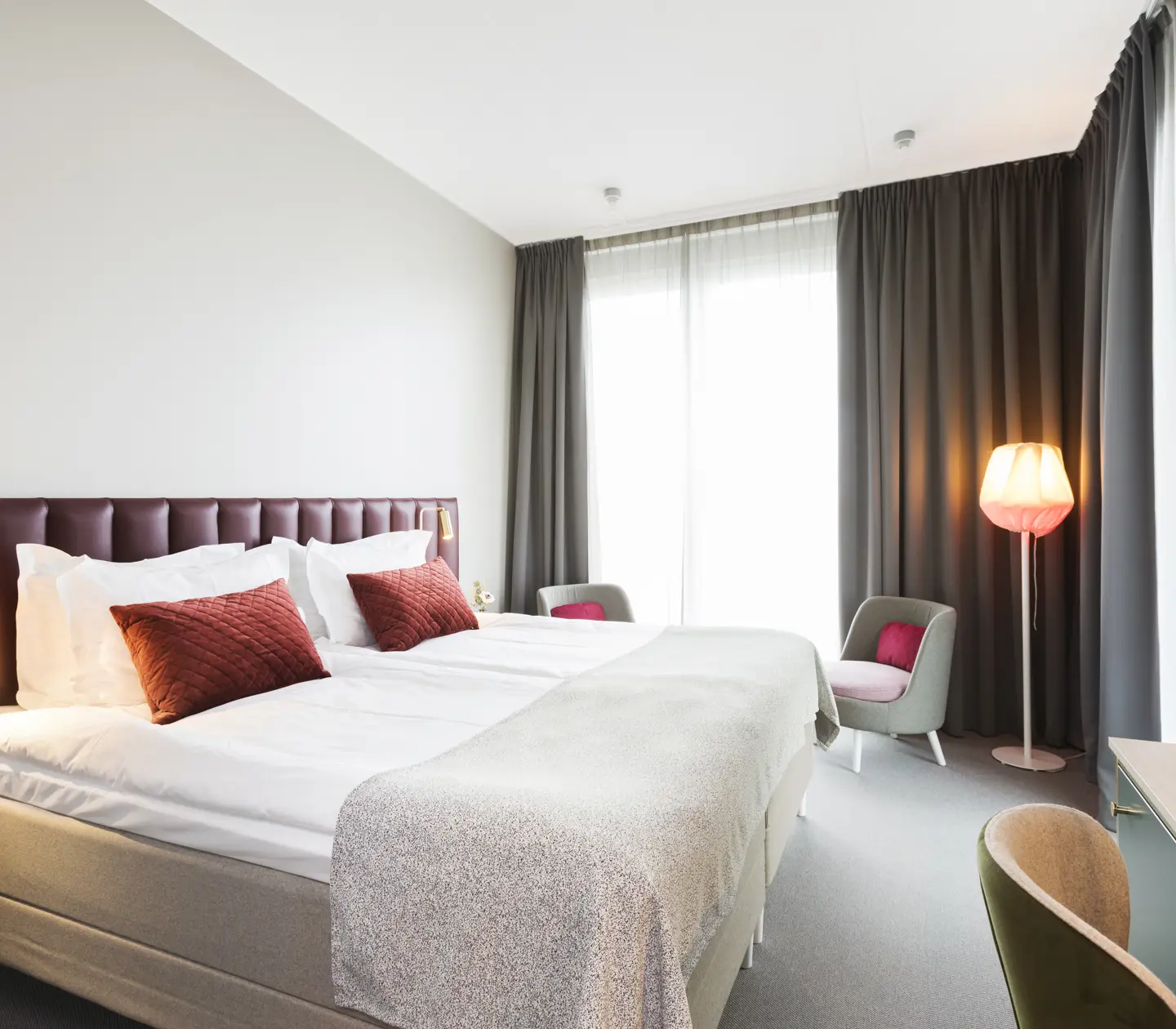 Ljust hotellrum med säng, vinröd sänggavel och stort fönster