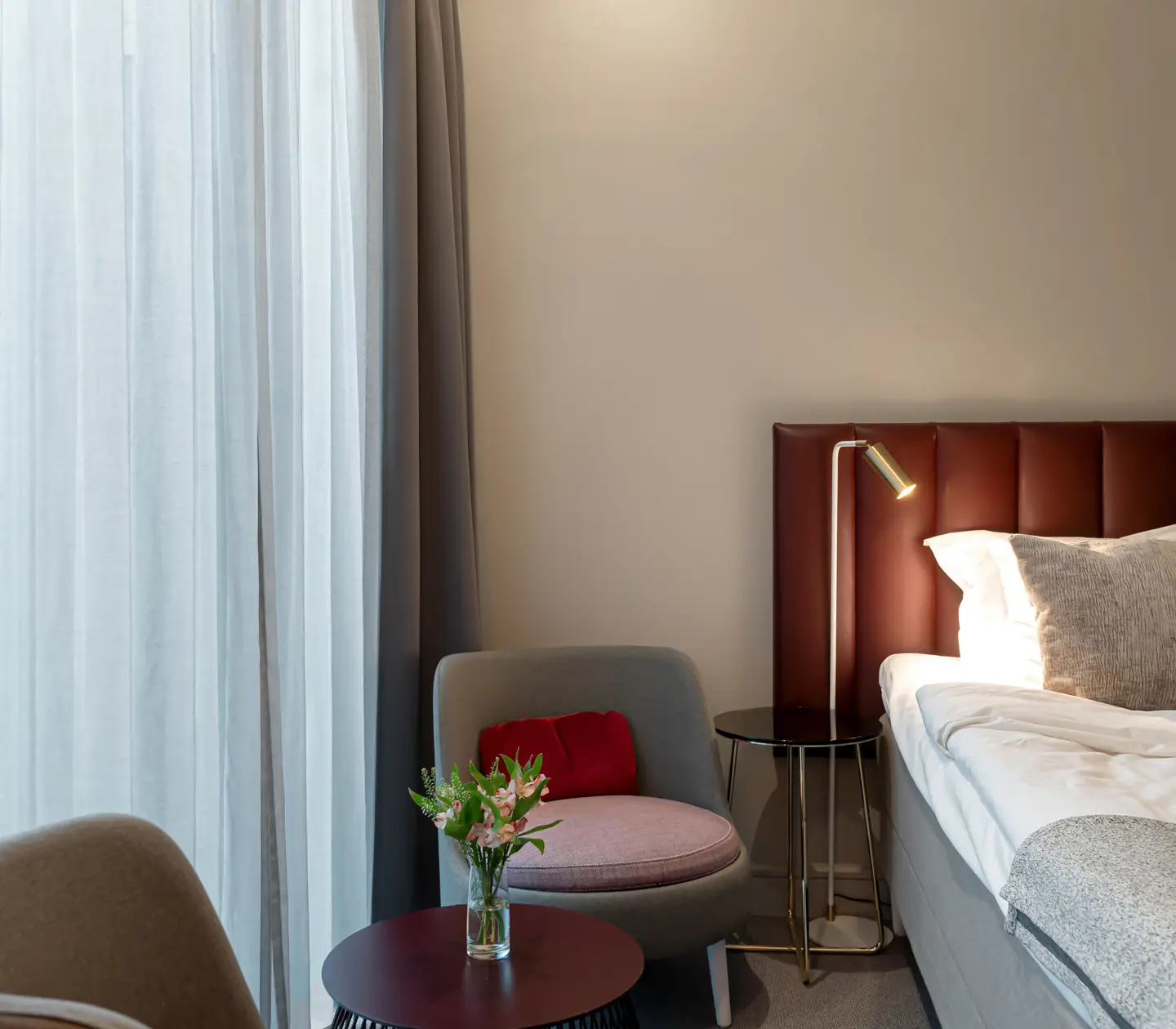 Ljust hotellrum med säng, vinröd sänggavel och fåtöljer