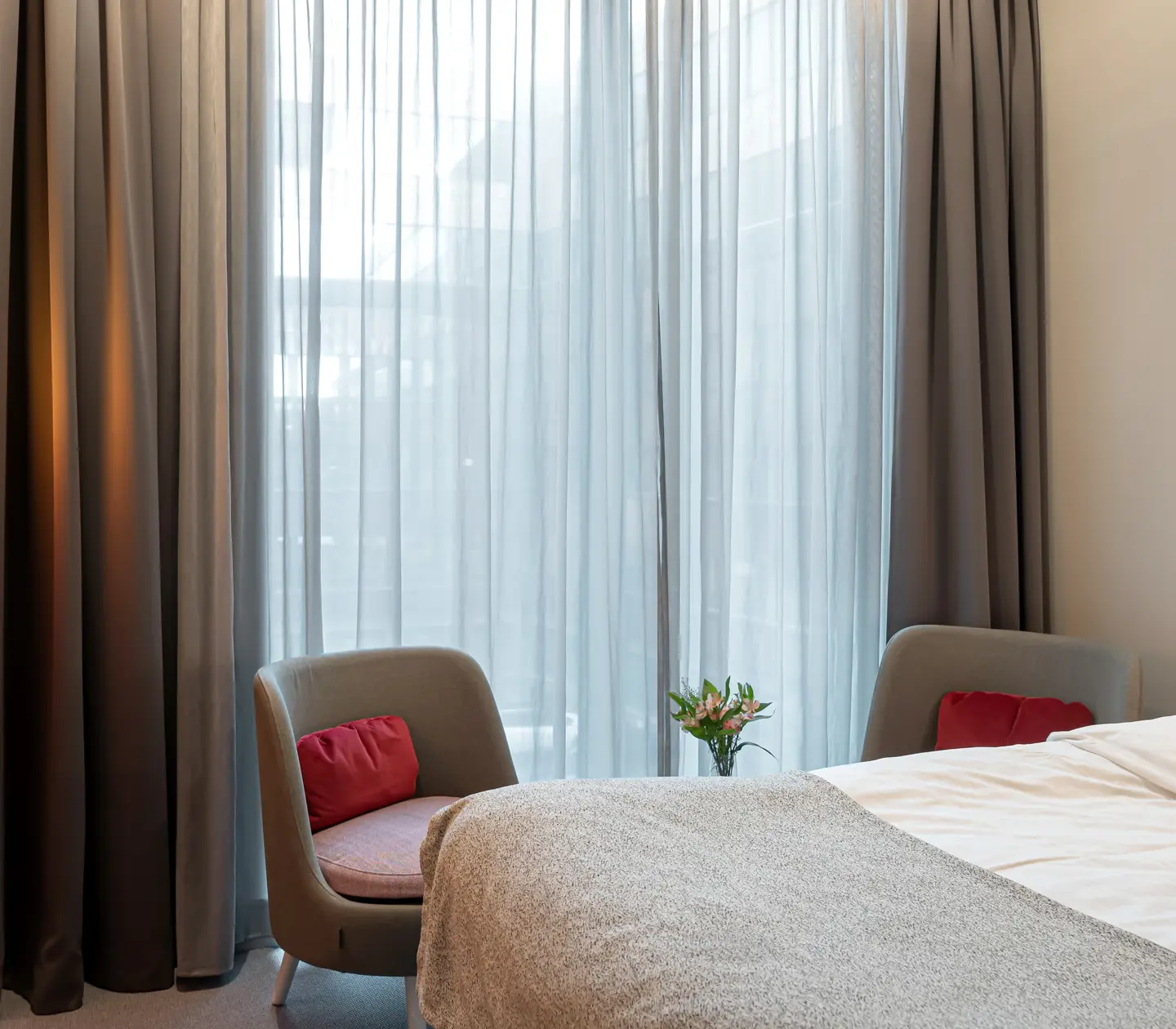 Ljust hotellrum med säng, stort fönster och fåtöljer