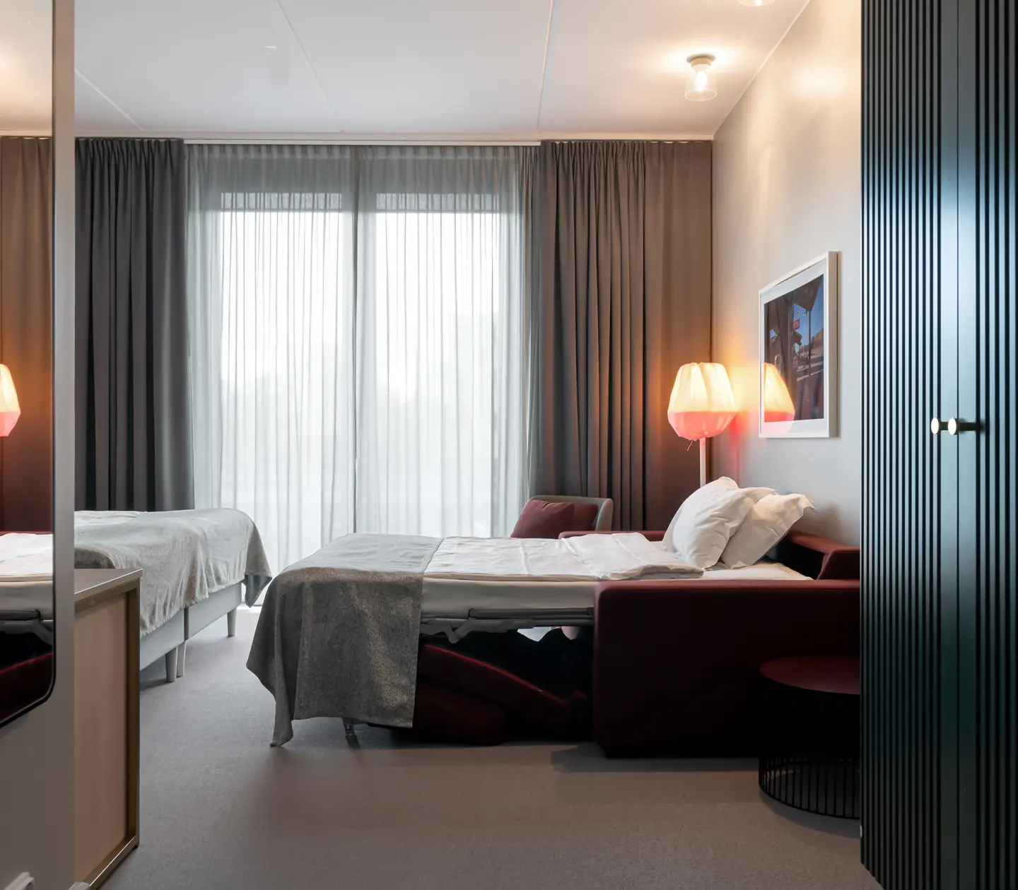 Ljust hotellrum med garderob, utbäddad bäddsoffa och stort fönster
