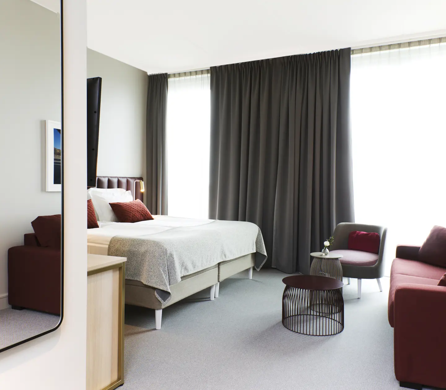 Ljust hotellrum med säng, röd soffa och stort fönster