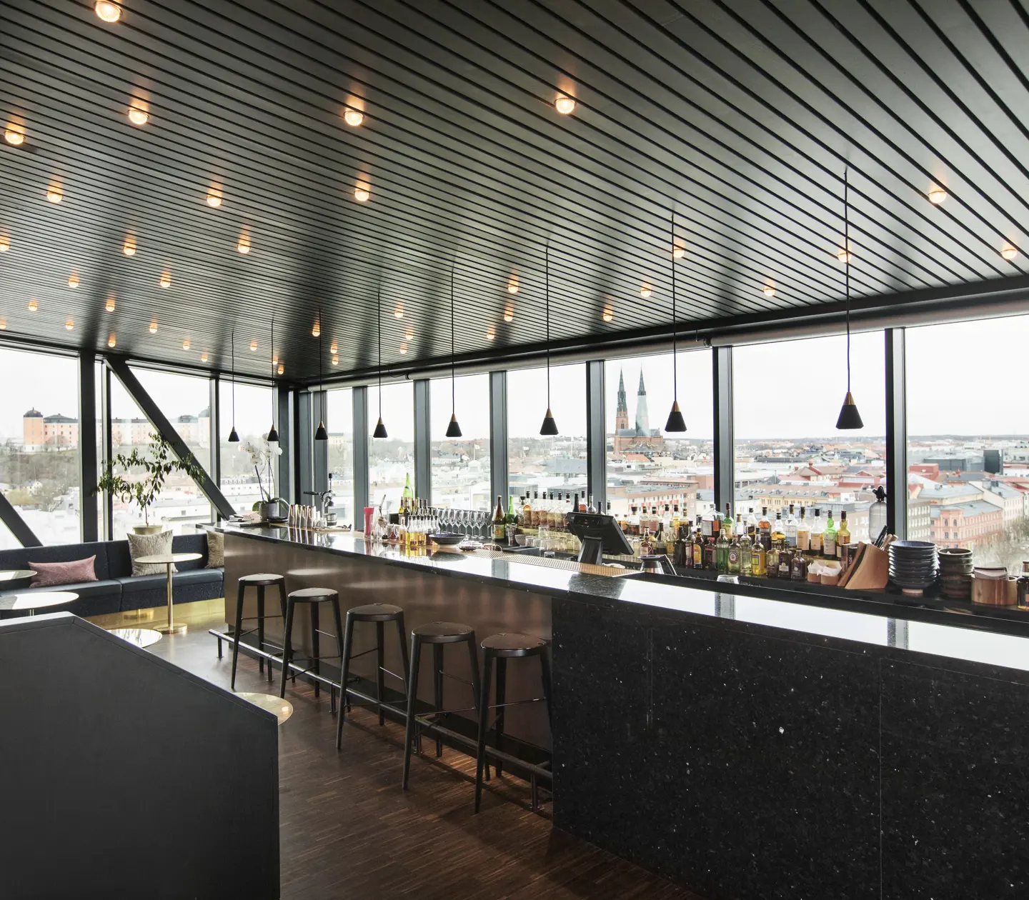 Restaurangmiljö med stor bar, taklampor och fönster längs väggarna med utsikt över Uppsala