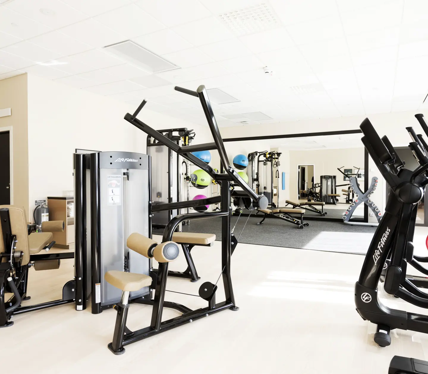 Gymmiljö med träningsmaskiner, speglar och medicinbollar