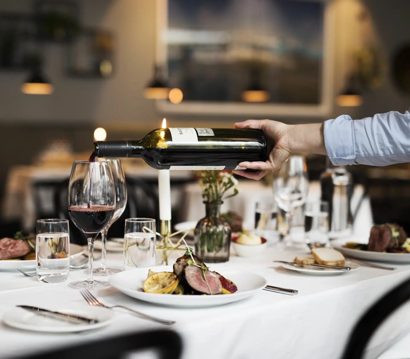 Middag serverad för fyra med mat på tallrikarna och rödvin som hälls i vinglas