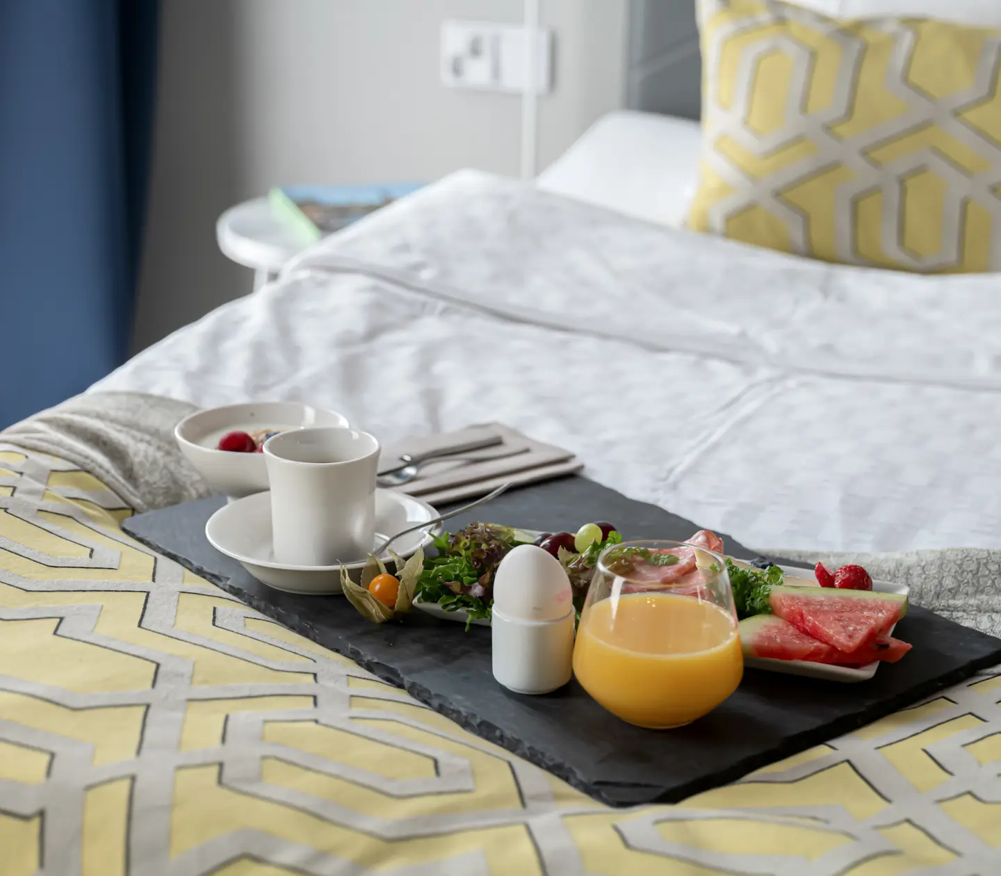 Frukostbricka med juice, ägg och frukt serverad på hotellsäng