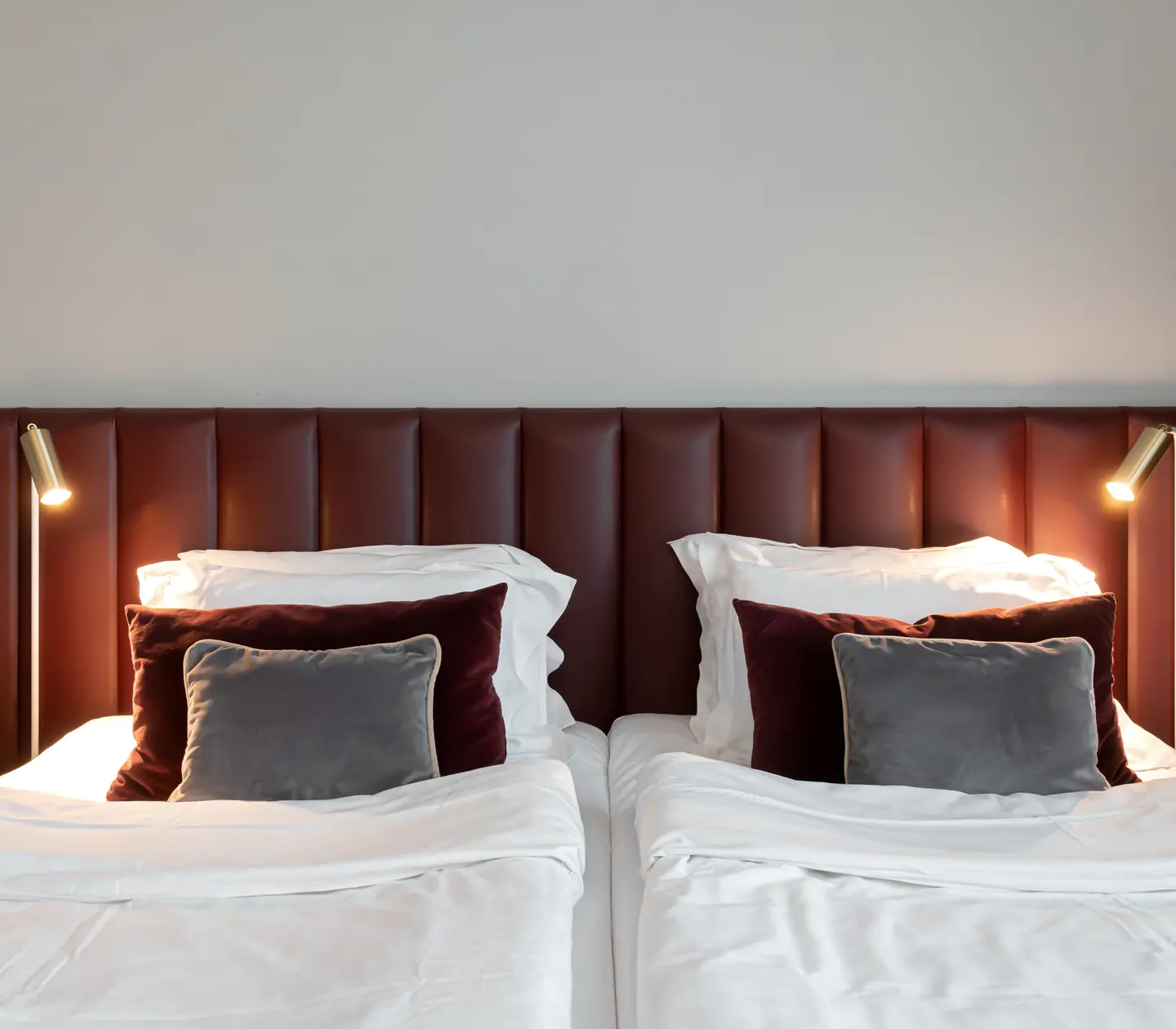 Hotellrum med säng, vinröd sänggavel och små sänglampor