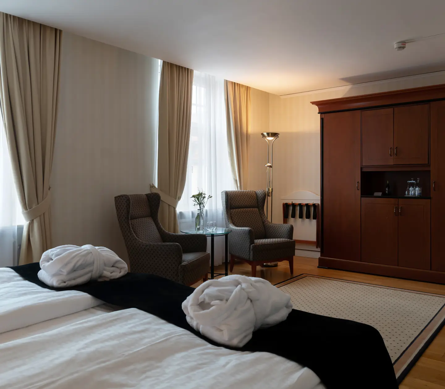 Mysigt hotellrum med morgonrock på säng, garderob och fåtöljer