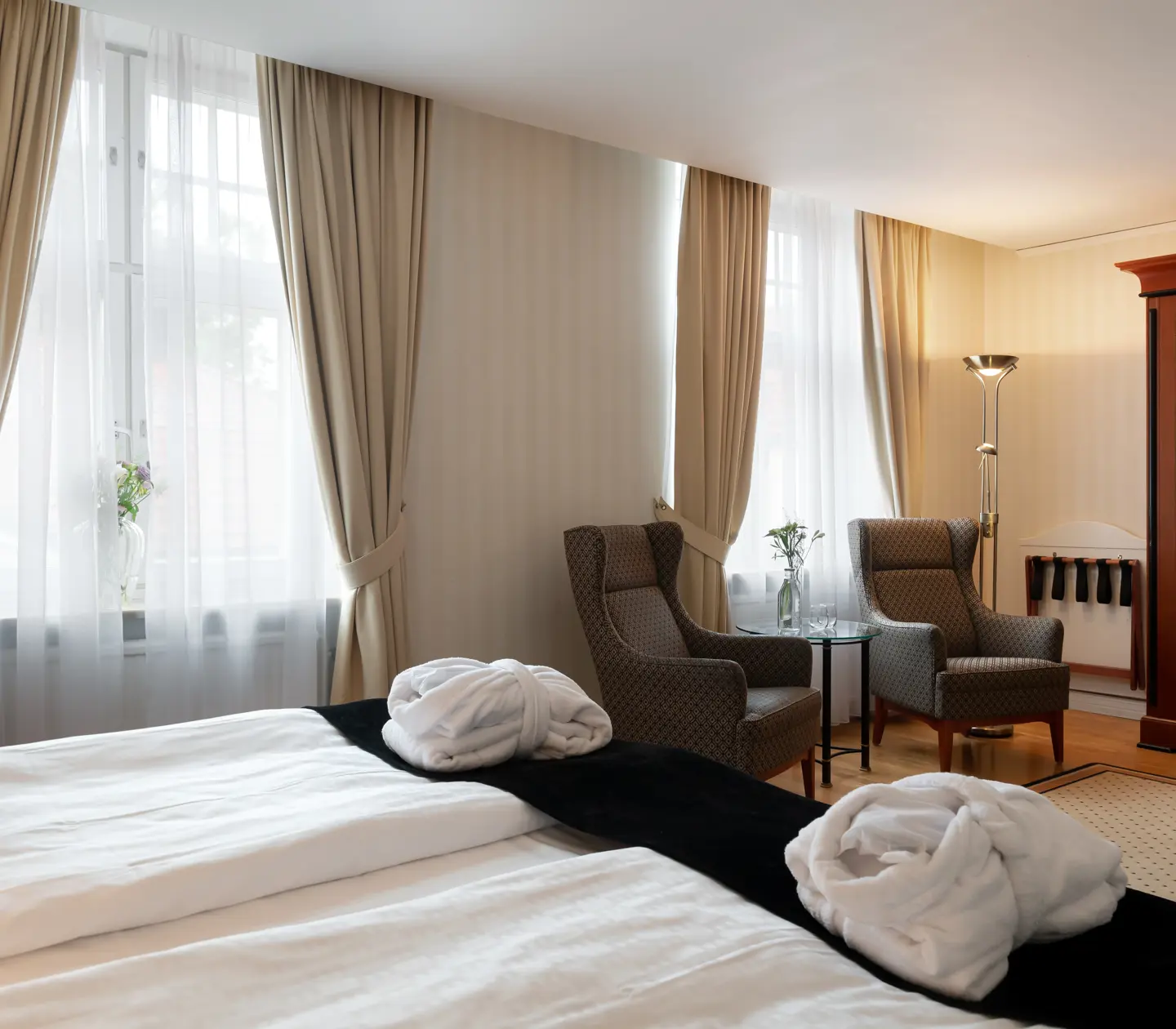 Stort hotellrum med morgonrockar på säng, fåtöljer och fönster