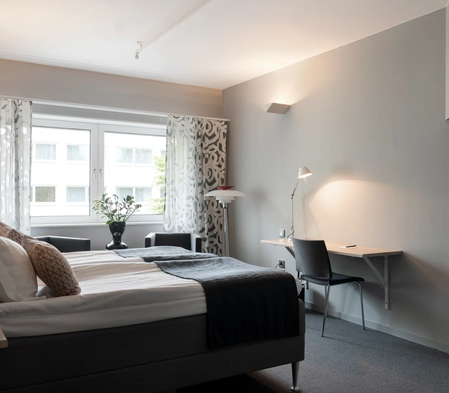 Ljust hotellrum med dubbelsäng, skrivbord och fönster