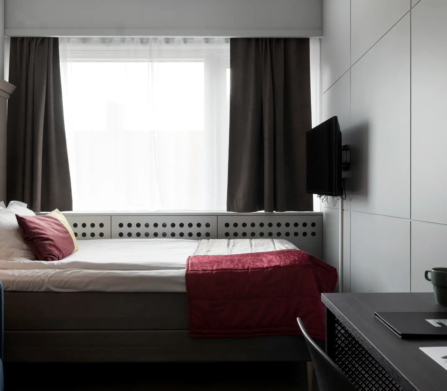 Stilrent hotellrum med enkelsäng, skrivbord och fönster