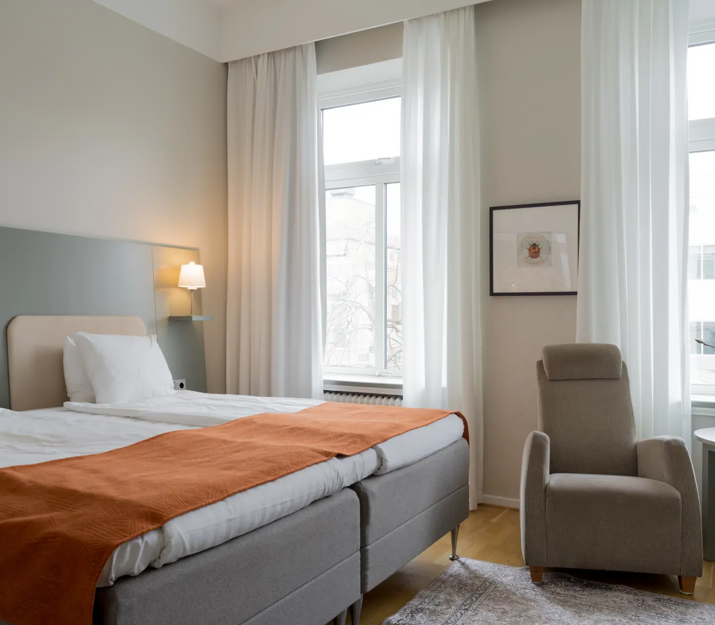 Ljust hotellrum med dubbelsäng, fåtölj och fönster