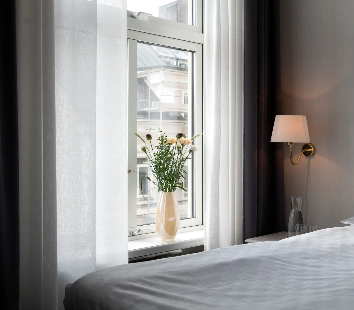 Ljust hotellrum med dubbelsäng, fönster och bukett