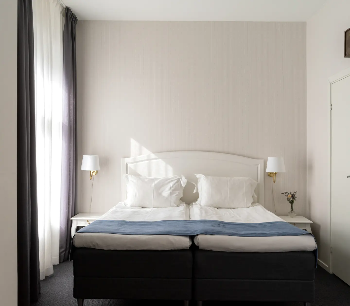 Ljust hotellrum med dubbelsäng, fönster och sänglampor
