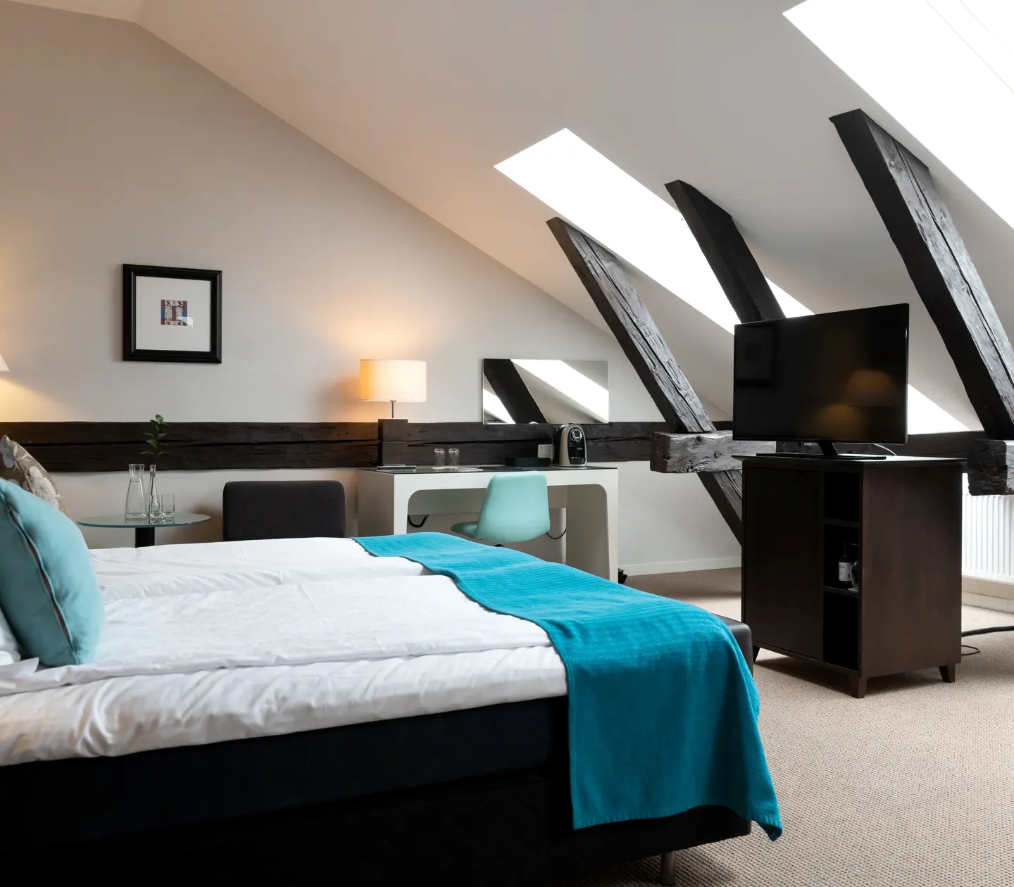 Hotellrum med träbalkar, snedtak, dubbelsäng och skrivbord