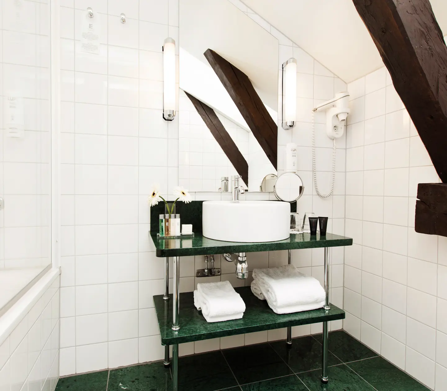 Ljust badrum med grönt golv, handfat, badkar och takbalkar