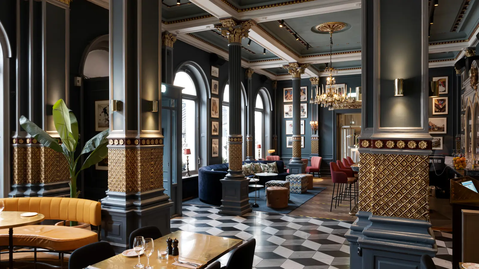 Elegant hotellobby med klassisk inredning, marmorgolv och höga kolonner. Ljus och rymlig atmosfär med sittplatser, dekorativa växter och en stor ljuskrona.
