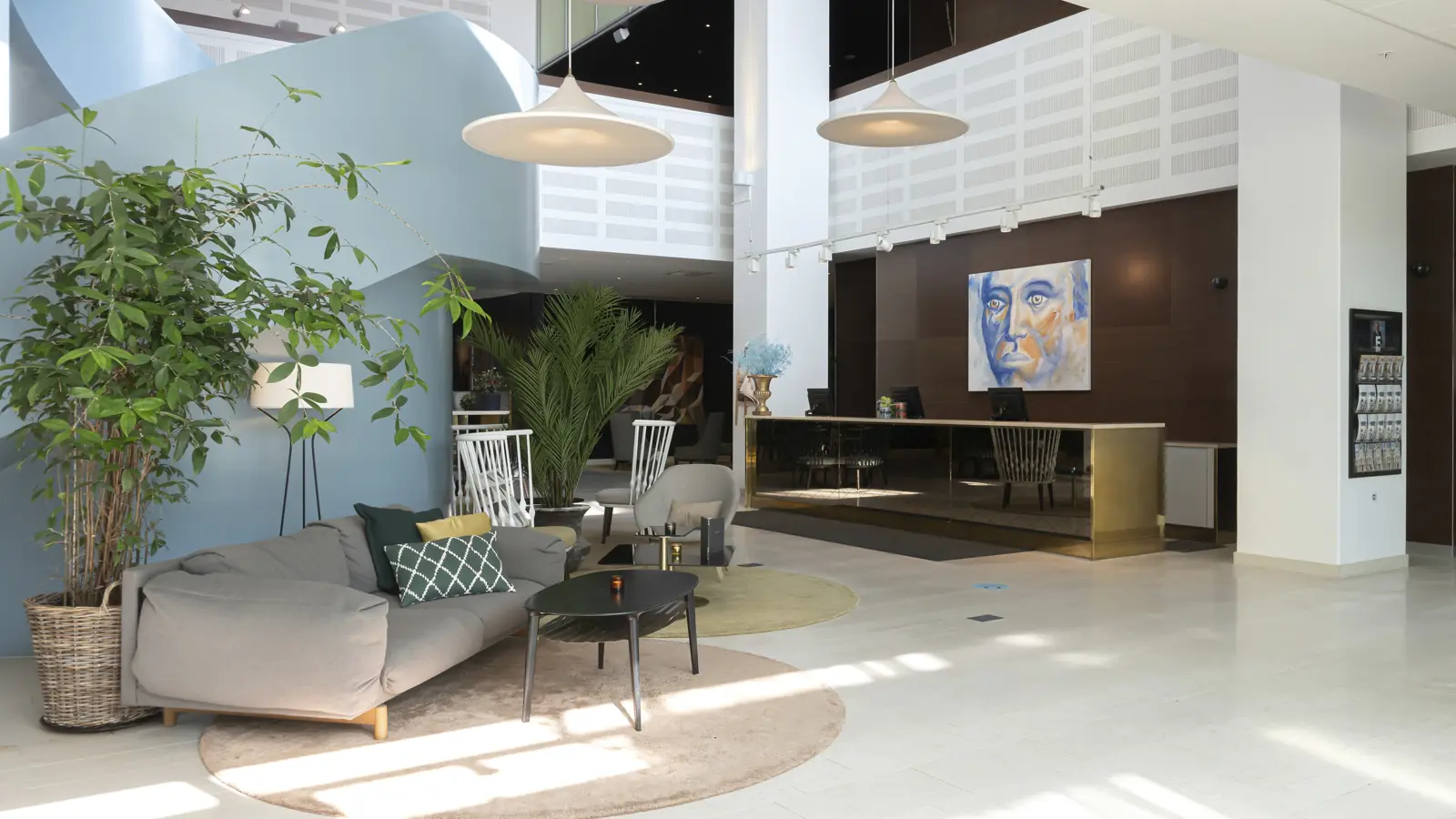 Modern hotellobby med stilrena fåtöljer, konst på väggen och en elegant reception med en spegelpolerad disk.